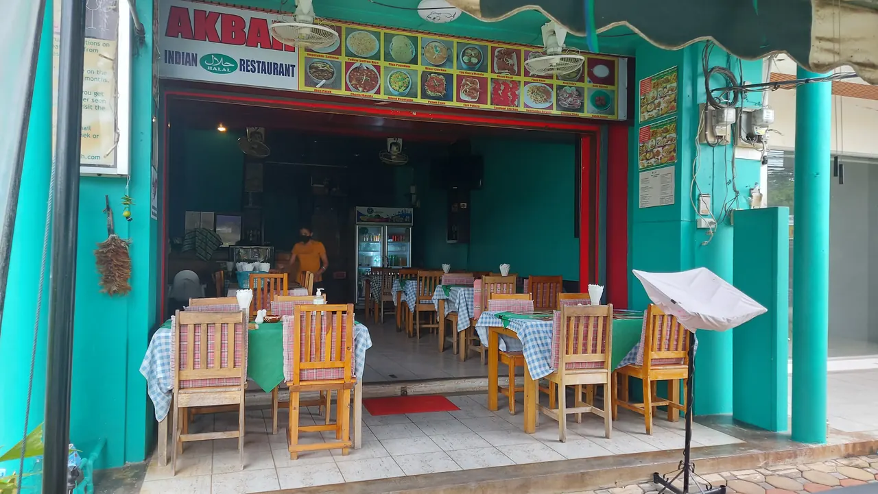 The teal shopfront by day, with the older AKBAR fascia, a strip of dish photos and tables inside