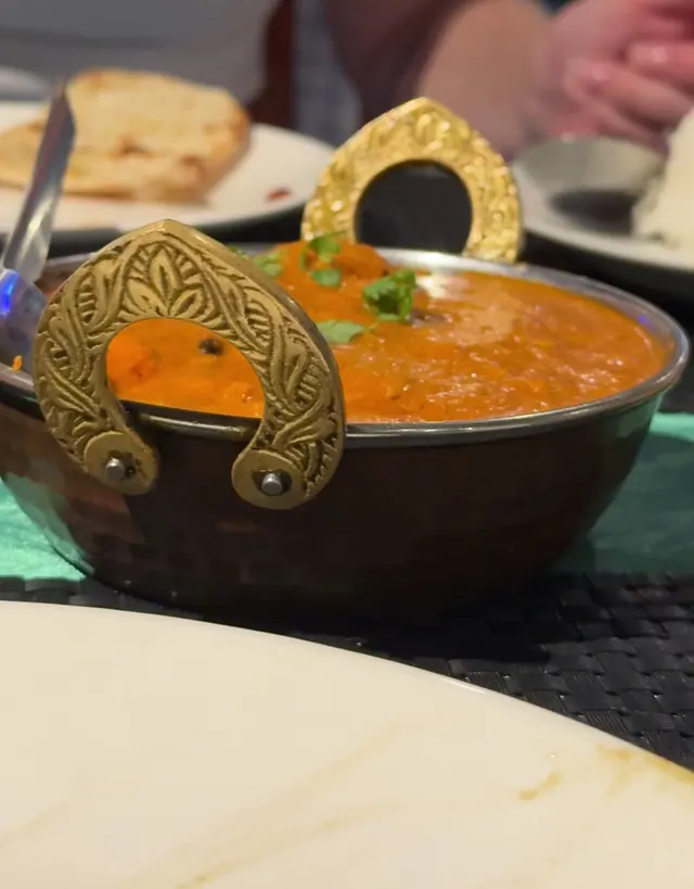 An orange curry in a brass karahi with ornate handles