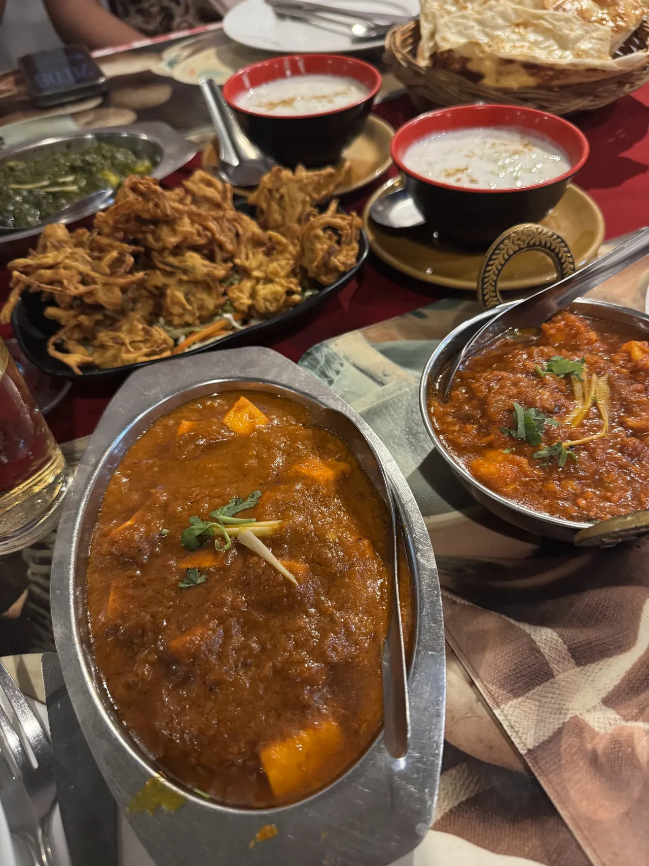 A table of dishes: curries, raita, fritters and a basket of naan