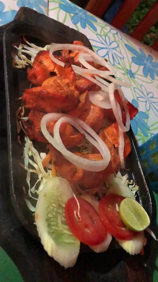 Tandoori pieces on a sizzling platter with onion rings, tomato and lime