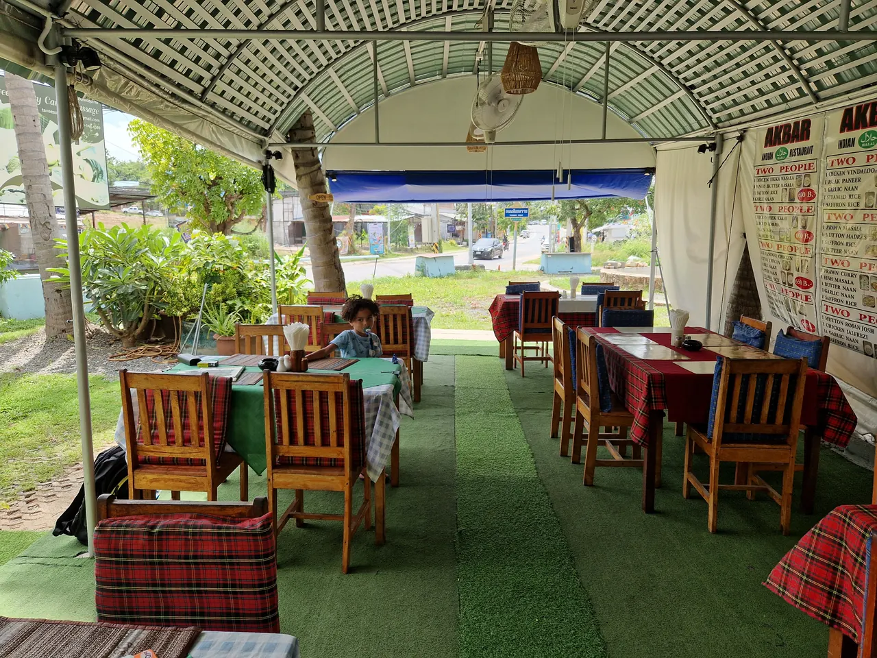 The covered garden terrace: tent roof, green turf, wooden chairs and red check tablecloths