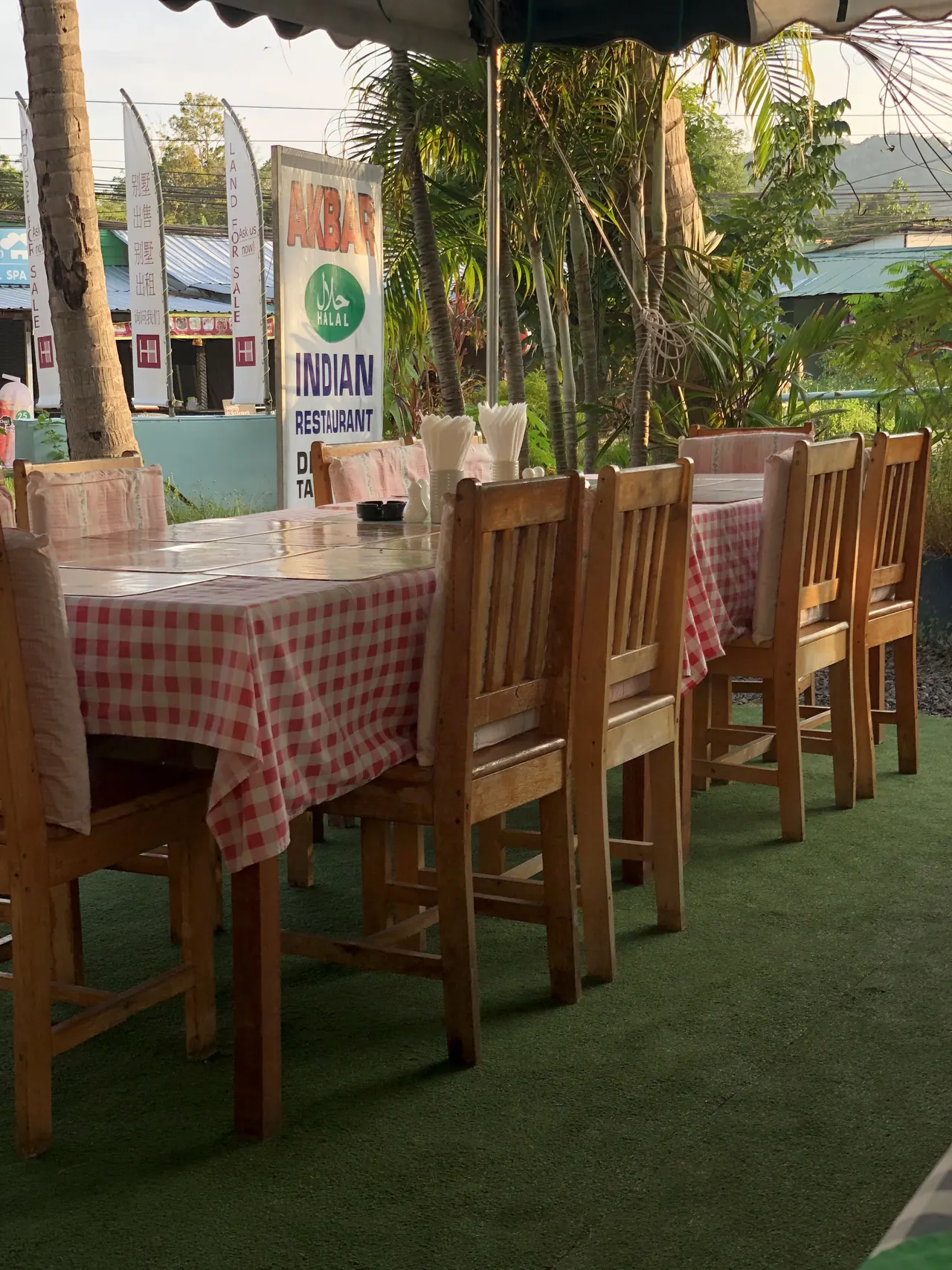 A row of tables with red check cloths on the terrace, with Akbar's standing sign behind